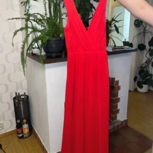 Röd långklänning från SisterS Point - Säljer en fantastisk röd långklänning från SisterS Point. Klänningen har en v-ringad design och är ärmlös, perfekt för festliga tillfällen. Den är i ett lätt och flödande material som ger en elegant look. Passar perfekt för sommarens alla fester!