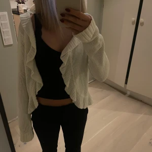 Vit stickad kofta med volangdetaljer - Säljer en superfin vit stickad kofta med volangdetaljer framtill. Den har långa ärmar. Koftan är i bra skick. Vet tyvärr inte vart den är ifrån då jag köpt den begagnad. Pris kan ändras