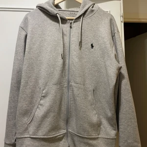 Grå hoodie från Polo Ralph Lauren - Säljer en snygg och bekväm grå hoodie från Polo Ralph Lauren. Den har en dragkedja framtill och en klassisk logga på bröstet. Perfekt för både vardag och chill. Den är nyskick, men tvättlappen på insidan saknas. Pris ej hugget i sten! Skriv om ni har frågor eller funderingar!!!
