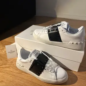 Säljer ett par snygga Valentino Open sneakers i vitt skinn med svarta detaljer. Skorna har coola nitar på sidorna och en klassisk snörning. Perfekta för både vardag och fest! De är i nytt skick och kommer med originalkartong.