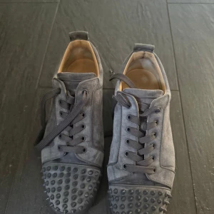 Grå sneakers med nitar från Christian Louboutin - Säljer ett par grå sneakers från Christian Louboutin i bra skick. Lite slitage på sulan men annars nästan nyskick. Box ingår, äkta 