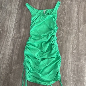 Grön klänning med rynkdetaljer - Snygg grön klänning med rynkdetaljer på sidorna som ger en cool look. Perfekt för sommardagar eller en avslappnad fest. Axelbandslös design och kort längd gör den både bekväm och trendig. Passar perfekt för en dag på stranden eller en somrig utflykt. 💚