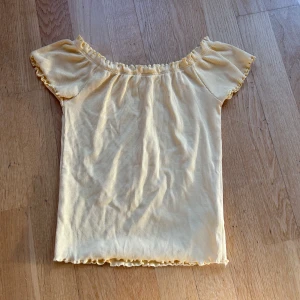 Gul ribbad topp från Gina Tricot - Säljer en söt gul ribbad topp från Gina Tricot i storlek S. Den har en offshoulder-design med volangdetaljer vid hals och ärmslut. Perfekt för sommardagar eller en avslappnad vårlook. Toppen är i mycket bra skick och redo för en ny garderob! 🌼