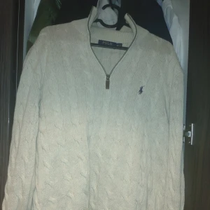 Polo Ralph Lauren - Säljer en snygg beige stickad tröja från Polo Ralph Lauren. Den har en dragkedja framtill och det klassiska logotypbroderiet på bröstet. Perfekt för höst och vinter, med en mysig och stilren look. Passar både till vardags och lite finare tillfällen. Skick:8/10