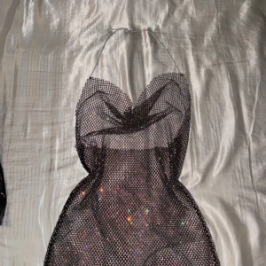 Glittrig axelbandslös klänning - Säljer en superglittrig och festlig axelbandslös klänning. Perfekt för en utekväll eller nyårsfest! Den har en tight passform och är täckt med glittrande paljetter som fångar ljuset. Klänningen är kort och har en elegant drapering framtill. Ett måste för den som vill sticka ut!