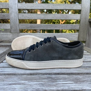 Grå sneakers från Lanvin - Säljer ett par stiliga grå sneakers från Lanvin i bra skick. Skorna har en snygg kombination av mocka och glansigt skinn med svarta snören. Perfekta för både vardag och fest! Sulan är vit och har lite slitage, men inget som påverkar användningen.Storlek Uk7 på lanvins motsvarar detta runt 42,5-43.