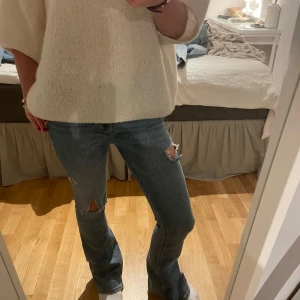 Blå jeans med slitningar - Säljer ett par snygga blå jeans med slitningar på knäna. De har en bootcut-stil och är lågmidjade, vilket ger en avslappnad och trendig look. Perfekta för både vardag och fest! 🕺