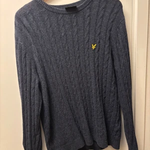 Mörkblå stickad tröja från Lyle & Scott - Säljer en snygg mörkblå stickad tröja från Lyle & Scott i storlek L. Tröjan har ett diskret kabelstickat mönster och en gul logga på bröstet. Perfekt för kyliga dagar och passar både till vardags och lite finare tillfällen. Den är gjord av 60% bomull och 40% ull, vilket gör den både varm och bekväm.