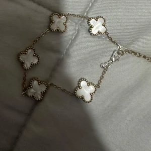 Armband med fyrklöverdesign - Snyggt armband med fem fyrklöverformade hängen i vit och guld. Perfekt för att ge en elegant touch till vilken outfit som helst. Kedjan är fin och diskret, vilket gör det lätt att bära både till vardags och fest.