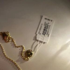 Guldigt Micheal Kors halsband - Snyggt guldigt halsband med ett unikt hängsmycke. Perfekt för att ge en touch av elegans till vilken outfit som helst. Halsbandet har en fin kedja och ett dekorativt lås. Passar både till vardags och festliga tillfällen.