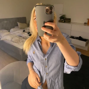 Blå skjorta med knappar - Säljer en snygg blå skjorta med knappar framtill. Skjortan har en normal passform och är perfekt för både vardag och fest. Den är tillverkad i ett bekvämt material och har långa ärmar som kan rullas upp för en mer avslappnad look.