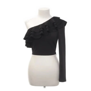 Svart oneshoulder topp med volang - Svart oneshoulder topp med volangdetaljer. Dragkedja på sidan. Använd 1 gång, väldigt bra skick. Pris kan diskuteras
