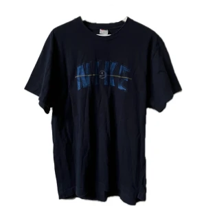 Vintage Nike t-shirt - Säljer en mörkblå t-shirt från Nike i bra skick. Den har en cool blå logga på framsidan och är perfekt för vardagsbruk. T-shirten är kortärmad och gjord i mjukt material för extra komfort. Passar perfekt till jeans eller shorts!
