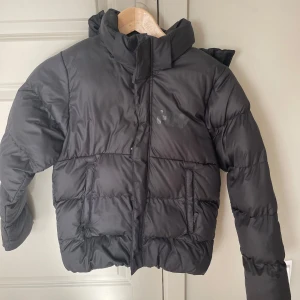 Svart pufferjacka från Helly Hansen - Säljer en svart pufferjacka från Helly Hansen i bra skick. Jackan är perfekt för kalla dagar med sin tjocka vaddering och höga krage. Den har en dragkedja framtill och två praktiska fickor. Passar perfekt för vinter och höst!