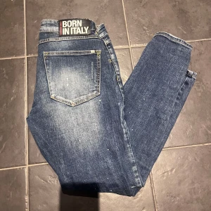 Blå jeans med slitningar  - Säljer ett par snygga blå jeans från Born in Italy zavetti . De har en cool slitningseffekt på framsidan och en klassisk femficksdesign. Perfekta för en avslappnad stil. Passar bra till både vardag och fest!