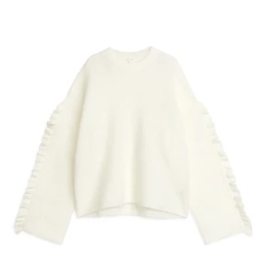 Vit stickad tröja med volangdetaljer - Superfin vit stickad tröja med volangdetaljer längs ärmarna. Perfekt för kyliga dagar när du vill vara både varm och stilren. Tröjan har en lös passform och långa ärmar, vilket gör den idealisk för både höst och vinter. Ett måste i garderoben för den som älskar mysiga plagg! Helt ny med lapp kvar!!(slutsåld på hemsidan)