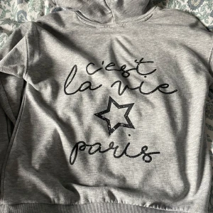 Grå hoodie med text⭐️ - Säljer en supermjuk och bekväm grå hoodie med texten 'c'est la vie Paris' och en stjärna på framsidan. Perfekt för en avslappnad dag eller en mysig kväll. Den har långa ärmar och en klassisk huva. Passar perfekt till jeans eller leggings! Jätte trendig och använd 1 tillfälle❤️