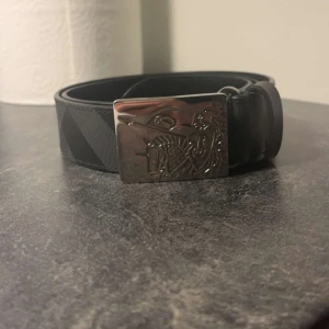 Svart bälte från Burberry - Säljer ett stilrent svart äkta bälte från Burberry i skinn. Bältet har ett coolt spänne med ett ingraverat motiv. Perfekt för att ge en lyxig touch till vilken outfit som helst. Tillverkat i Italien och i mycket bra skick. Nypris 5-6 säljer för runt 2000, pris kan diskuteras. Varan är i oanvänt skick, som helt ny då jag ej använder byxor som kräver bälte mer än 2 gånger sen jag köpte bältet.