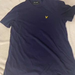Mörkblå t-shirt från Lyle & Scott - Snygg mörkblå t-shirt från Lyle & Scott med ett gult broderat emblem på bröstet. Perfekt för en avslappnad stil.