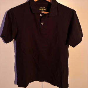 Svart pikétröja från Race Marine - Snygg svart pikétröja från Race Marine Essentials. Tröjan har korta ärmar och knappar framtill. Perfekt för en stilren look. I väldigt bra skick. 