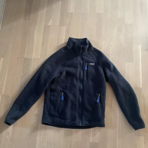 Blå fleecejacka från Patagonia. storlek s  - Säljer en blå fleecejacka från Patagonia med dragkedja och hög krage. Jackan har tre fickor med dragkedjor och är perfekt för kyliga dagar. Den är långärmad och har en stilren design.