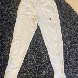 Beige träningsbyxor från Nike - Säljer ett par vita byxor från Nike med Dri-FIT-teknologi. Byxorna har en elastisk midja och ett litet broderat Nike-märke på benet. Perfekta för träning eller en avslappnad dag.