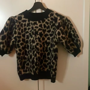 Leopardmönstrad tröja från NA-KD - Snygg leopardmönstrad tröja från NA-KD i svart och beige. Tröjan har puffiga trekvartsärmar och en rund halsringning. Perfekt för att ge din outfit en trendig touch. 🐆