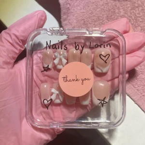 Rosa och vita lösnaglar med dekorationer - Snygga lösnaglar i rosa och vitt med fransk manikyr. Två naglar har en söt rosett i vitt. Perfekt för en personlig och stilren look. Handgjorda. 