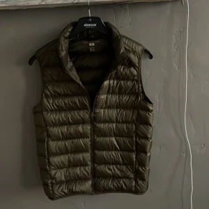 Olivgrön Uniqlo Väst - Säljer en olivgrön dunväst från Uniqlo. Västen är ultralätt och har en dragkedja framtill. Perfekt för lager-på-lager under kyliga dagar.