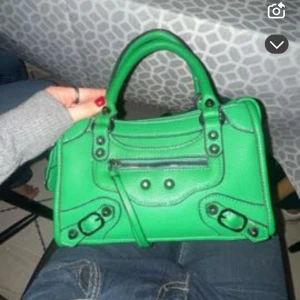 Grön handväska med dragkedja - Snygg grön handväska med coola detaljer och dragkedja framtill. Perfekt för att ge en färgklick till din outfit. Den har dubbla handtag och stilrena knappar.