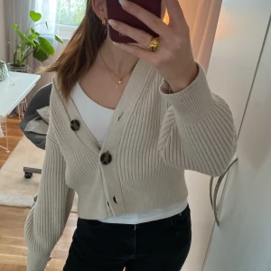 Beige ribbad kofta från H&M (kontakta mig innan köp) - Säljer en snygg beige ribbad kofta från H&M med stora knappar framtill. Perfekt för lager-på-lager och har en skön passform med långa ärmar. Ett måste i garderoben för en stilren look.