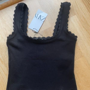 Svart linne från Zara - Snyggt svart linne från Zara med dekorativa kanter. Perfekt för en stilren look. Nytt med prislapp kvar. Hör av dig om di har några frågor!