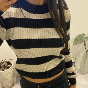 Randig ribbad tröja - Säljer en snygg randig tröja med breda svarta och beige ränder. Tröjan är ribbad och har en croppad passform med långa ärmar. Perfekt för en stilren look!
