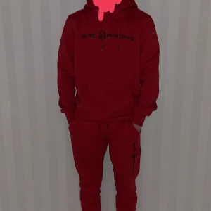 Röd sail racing tracksuit - Snygg röd mjukis dress ifrån Sail Racing med en bekväm passform. Denna kombination med byxa och hoodie passar perfekt för alla årstider. Hoodien är som ny och byxorna lika så, jag har enbart använt hoodien ett fåtal gånger. På bilden ovan var jag 168cm och då passade både byxorna och hoodien perfekt. Nypris: 1800kr. Hör gärna av dig vid funderingar. Köparen står för frakten!