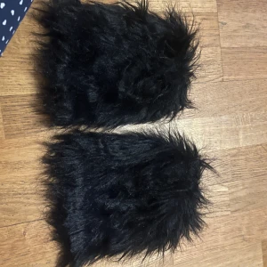 Svarta pälsiga benvärmare  - Säljer ett par unika svarta benvärmare med fluffig pälsdesign. Perfekta för att hålla fötterna varma och bekväma De har en mjuk och mysig känsla som gör dem idealiska för kalla dagar.