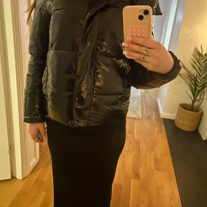 Svart pufferjacka från Calvin Klein Jeans - Snygg svart pufferjacka från Calvin Klein Jeans med glansig finish. Jackan har dragkedja och knappar framtill samt en hög krage för extra värme. Perfekt för kyliga dagar. Köptes för 2999kr.