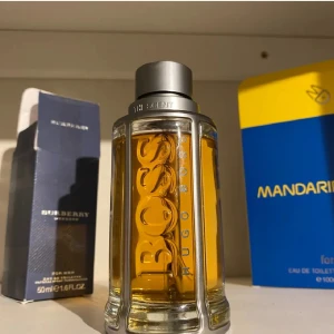 Parfym Hugo Boss The Scent - Elegant parfymflaska från Hugo Boss med en stilren design. Flaskan är genomskinlig med en metallisk kork och innehåller en gyllene doftvätska. Perfekt för den som söker en sofistikerad och maskulin doft.