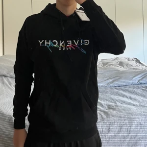 Svart hoodie från Givenchy - Snygg svart hoodie från Givenchy med färgglad logga på framsidan. Perfekt för en stilren och avslappnad look. Hoodien har en klassisk passform med långa ärmar och en bekväm huva. Köpt här på Plick passar mellan 177-185