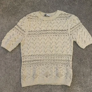Beige stickad tröja från Zara - Säljer en snygg beige stickad tröja från Zara med ett unikt mönster. Tröjan har trekvartsärmar och en rund halsringning. Perfekt för lager-på-lager-stil eller som ett statement-plagg i garderoben.