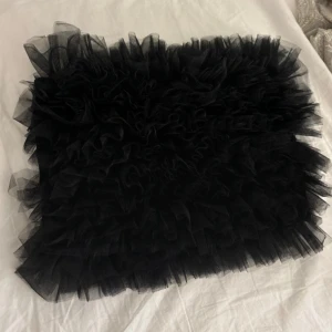 Svart tyllkjol - Snygg svart bandue topp i tyll med volangdetaljer. Perfekt för att ge en extra touch till din outfit. Toppen har en elastisk midja för bekväm passform.