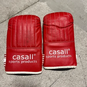 Röda boxningshandskar från Casall - Säljer ett par röda boxningshandskar från Casall med vit text och randiga handledsband. Handskarna har en vadderad design för extra skydd och komfort. Perfekta för träning och sparring. Pasar mellan åldern 11 år till 99+