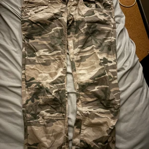 Cargobyxor i camouflage - Snygga cargobyxor i klassiskt camouflagemönster. Perfekta för en avslappnad och cool stil. Byxorna har flera praktiska fickor och en bekväm passform.