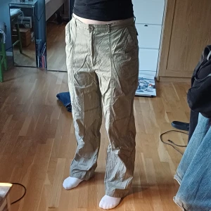 Beige cargobyxor - Säljer ett par beige cargobyxor med flera praktiska fickor och knappdetaljer. Byxorna har en loose passform och är perfekta för en avslappnad stil. Tunnt luftigt tyg. Jag är 167cm.