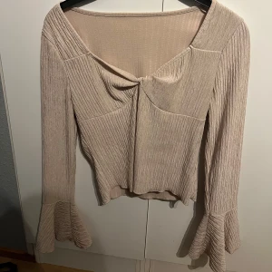 Beige ribbad topp med volangärmar - Snygg beige ribbad topp med långa volangärmar och en v-ringad design. Perfekt för en stilren look. Wow så sjukt fin på, perfekt till alla tillfällen. 