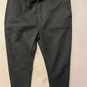 Svarta byxor från Smog - Snygga svarta byxor från Smog med en stilren design. Byxorna har en knapp och dragkedja framtill och är perfekta för en chic look. De är tillverkade i ett bekvämt material som passar till många tillfällen.