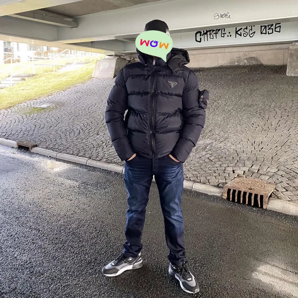 Snygg marinblå pufferjacka med huva och dragkedja av märket Prada. Jackan har en quiltad design och en logotyp på bröstet. Perfekt för kyliga dagar.. Takit.