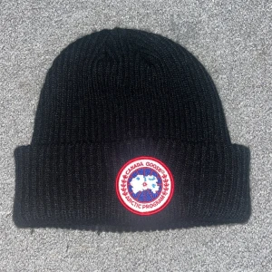 Svart ribbad mössa från Canada Goose - Snygg svart ribbad mössa från Canada Goose med ett broderat märke framtill. Perfekt för kalla dagar och ger en stilren look. Passar både till vardags och utomhusaktiviteter. Och köp nu priset är 300kr kommer inte gå ner mer än så😁