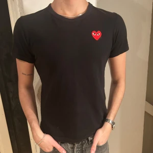 Svart t-shirt från CDG  - Snygg svart t-shirt med ett litet rött hjärta på bröstet. Perfekt för en stilren och enkel look. Kortärmad och i en bekväm passform. Storlek m men skulle säga att den passar s bättre. Från CDG, commes des garcons. 