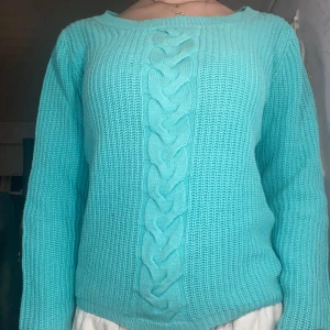 Turkos stickad tröja - turkos stickad tröja med flätmönster framtill. Tröjan har långa ärmar och en rund halsringning. Från ellos 