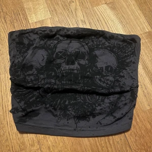 Svart tubtopp med dödskallemotiv - Snygg svart tubhalsduk med ett coolt dödskallemotiv. Perfekt för att ge din outfit en edgy touch. Tillverkad i mjukt material som håller dig varm under kyliga dagar.